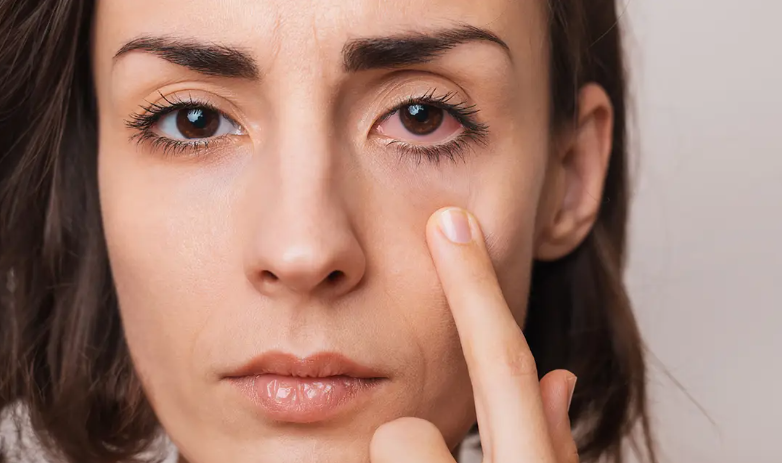 Close-up of a woman pointing to her eye with a finger